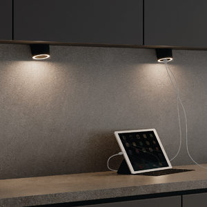 Two puck lights shine above a grey counter. On the right, an ipad is charging in one of the puck light's two USB ports.