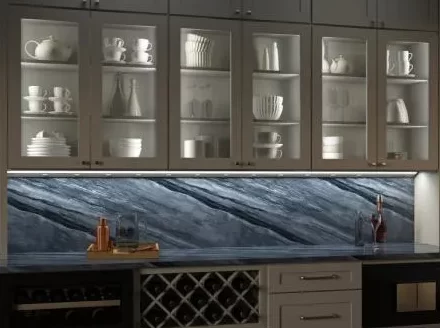 A cabinet with all-white dishware above a countertop with lighting from a long set of lighted powerstrips. The backsplash illuminated above the counter is blue and white marble.
