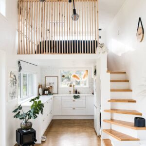 A tiny house with modern design elements such as white paint, light wood stairs, plants, and modern wall decor