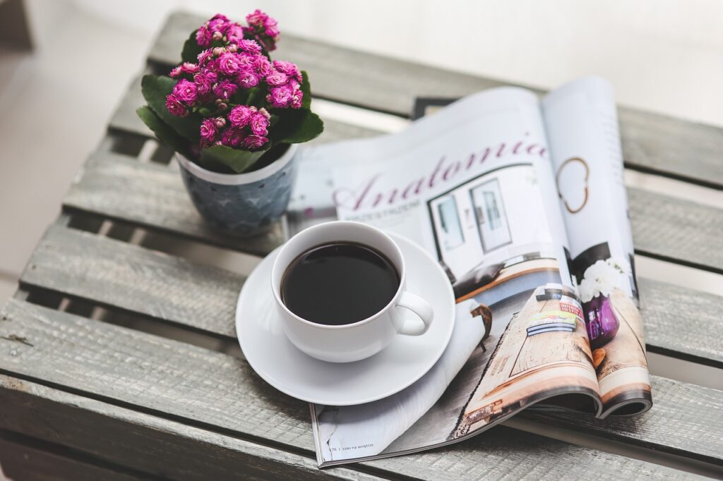A home renovation magazine on a coffee table with flowers and a cup of coffee.