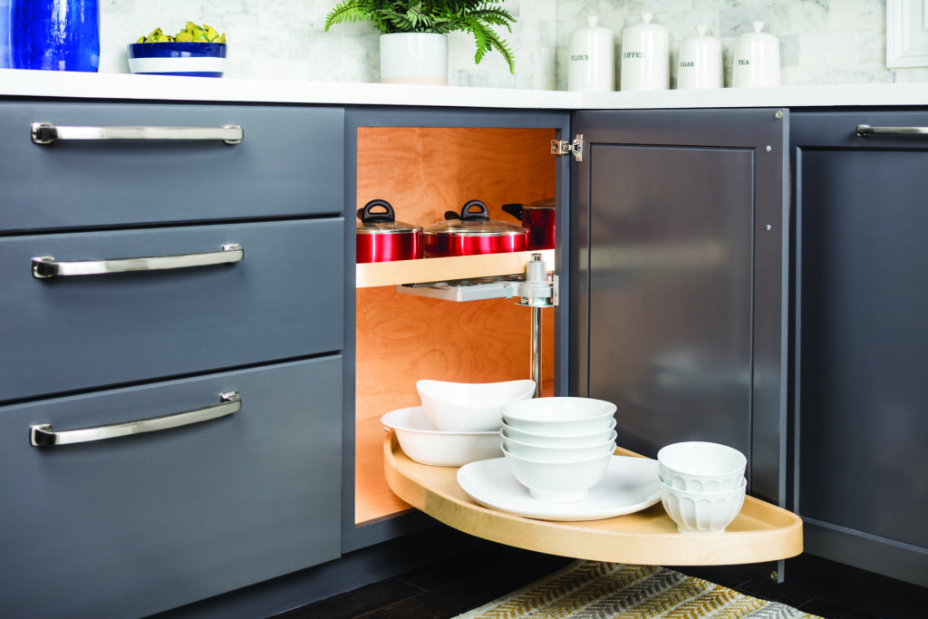 A half-moon kitchen storage swing-out, with one shelf out of the corner cabinet holding white ramekins and bowls