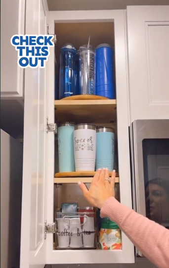 A clever kitchen storage solution where a 3-shelf, slim cabinet is organized with a lazy susan on two of the top shelves to allow for easier access to water bottles and tumblers