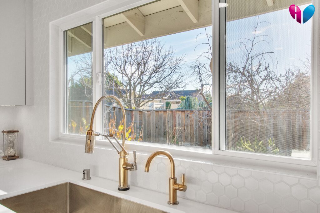 A golden touch faucet beneath a wide kitchen window